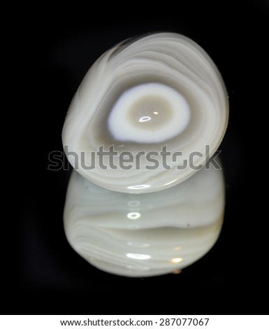 Polished mineral oval with reflection in a mirror on a black background