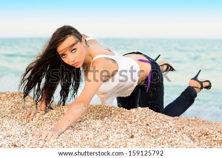 Sexy young brunette in wet clothes posing on the beach