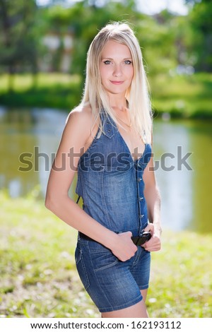 Sexy blonde in jeans clothes posing near the pond