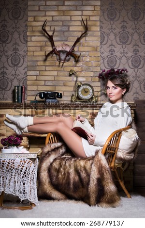Sexy woman in white socks and sweater posing on the chair with a book