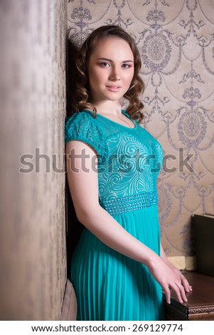 Portrait of young thoughtful woman posing in turquoise dress near the wall