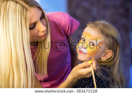 Pretty blond woman painting the face of a little girl