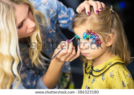 Young visagist painting the face of a little girl