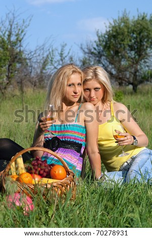 Two sensual blonde with wineglasses sitting on a grass