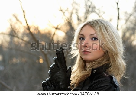 Blonde young woman with a gun at the sunset