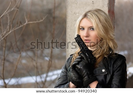 Scared young woman in leather jacket with a gun