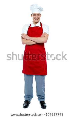 Handsome young cook posing in uniform with arms crossed, full length portrait
