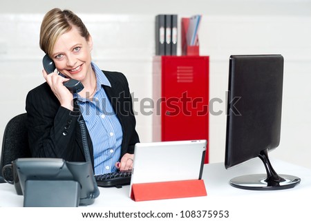 Smiling female secretary attending phone call and looking at camera