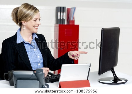 Female executive pointing at computer screen sitting on desk and working