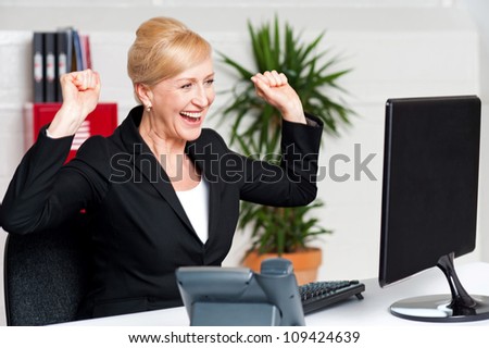 Excited corporate lady with raised arms looking at computer screen