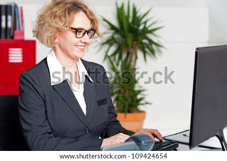 Aged woman in office wearing eyeglasses working on computer