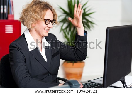 Smiling woman with raised arm looking at screen and typing on keyboard with other hand