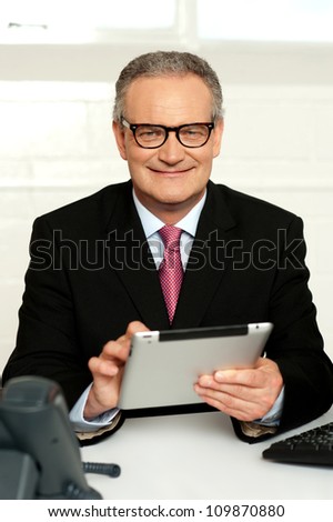 Senior executive sitting with tablet pc in hands and smiling at camera