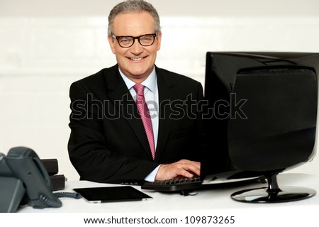 Happy aged corporate man typing on keyboard while looking at you