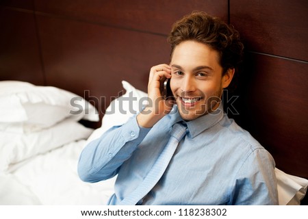 Cropped image of charming young man resting on headboard while talking on the phone