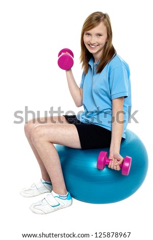 Pretty teen seated on a blue pilate ball doing dumbbells. Stay fit and healthy.