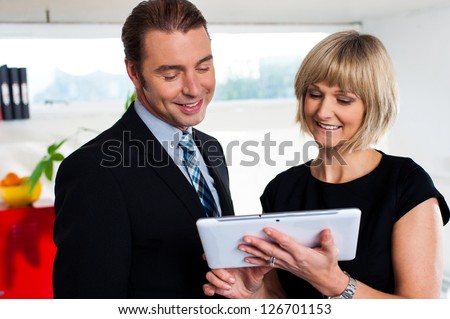 Boss with female secretary busy reviewing appointments saved on tablet device, office background.