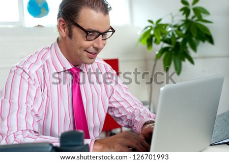 Smiling man in formals working on laptop inside office.