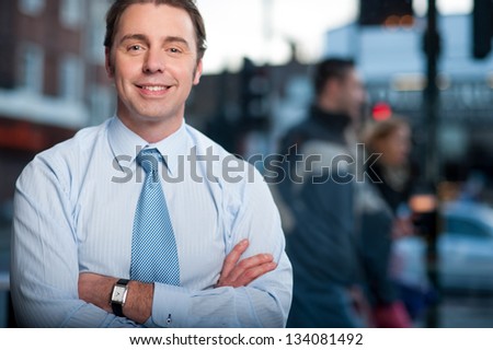 Friendly corporate guy posing with arms crossed. Street background.