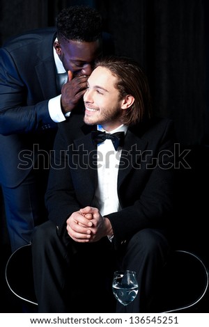 African guy whispering something into the ears of his boss during a party.