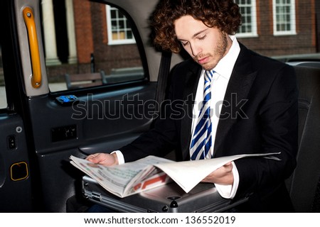 Handsome young businessman reading newspaper inside taxi cab.
