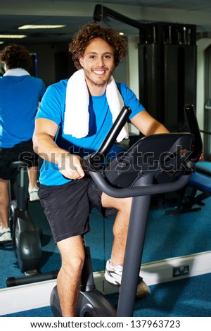 Handsome smiling young man cycling at the gym.