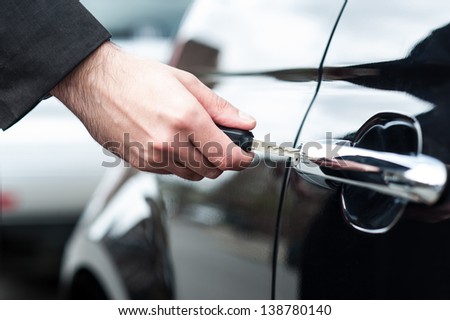 Closeup of a man\'s hand inserting key into the door lock of a car.