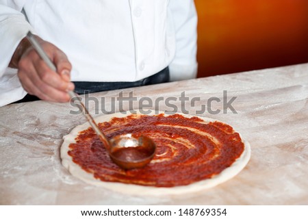 Chef preparing the pizza base with sauce