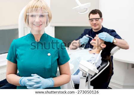 Assistant posing, dentist treating  patient behind