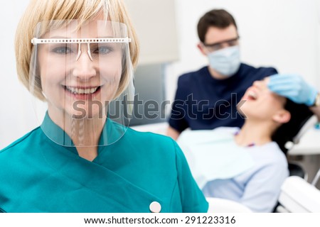 Woman assistant posing, behind dentist treating patient
