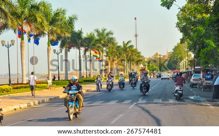 PHNOM PENH, CAMBODIA - MARCH 1, 2014: Traffic moves along Preah Sisowath Quay along the Tonle Sap riverfront with its parade of palms and international flags, heading toward Royal Palace Park.