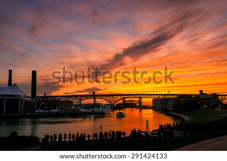 A silhouetted crowd of photographers lines the east bank of the Cuyahoga River in Cleveland to shoot the summer solstice sunset