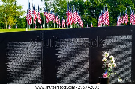 TWINSBURG, OH, USA - JULY 4, 2015: A field of flags is seen above a section of a replica Vietnam Memorial Wall, on tour with the Cost of Freedom tribute, a traveling veterans-based exhibit