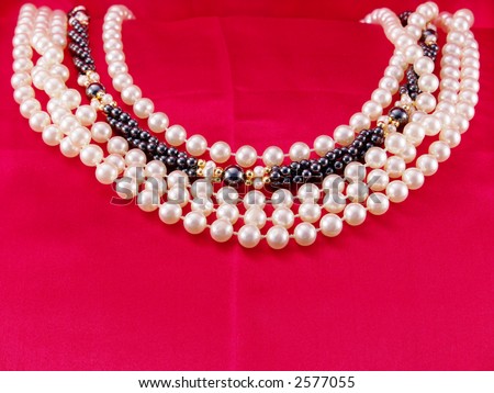 Strands of white pearls with one strand of black pearls on red fabric