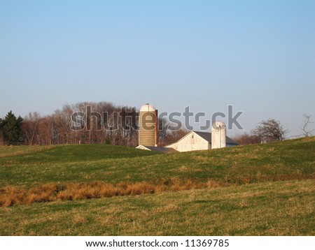 White barn and silos in late afternoon light behind rolling pasture