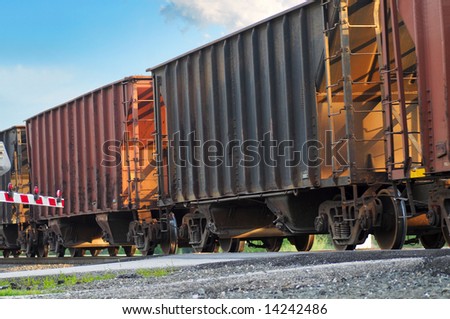 Freight cars rolling over a grade crossing with crossing gate lowered at left
