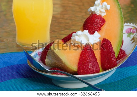 A fresh slice of melon garnished with strawberries and dollops of whipped cream on a fancy dish