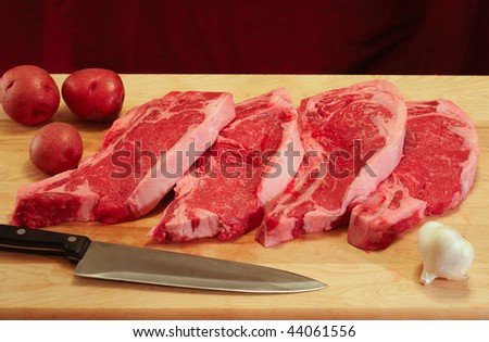 Four freshly cut strip steaks with red potatoes and garlic on a cutting board
