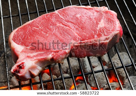 A strip steak newly placed on a charcoal grill
