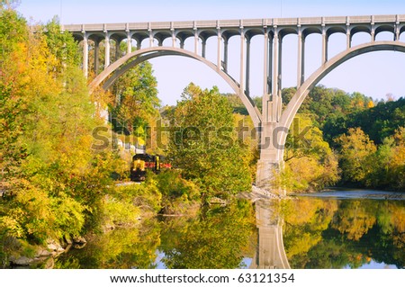 A locomotive passes under a high arch bridge in a scenic area