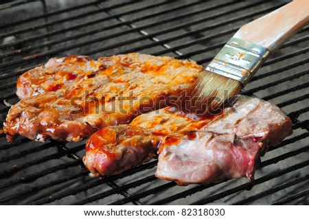 Two pork chops on a charcoal grill being brushed with bbq sauce