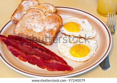 A breakfast of fried eggs, turkey bacon, toast, and juice