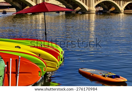 Kayak rentals stacked on dock with umbrella near bridge