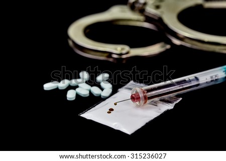 Heroin in a hypodermic needle  with packets of heroin powder, pills and hand cuffs isolated on black with shallow depth of field