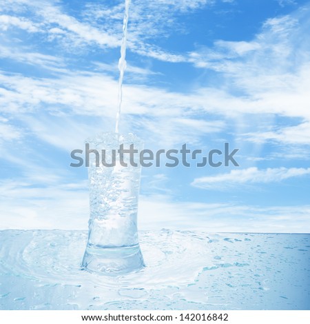 Glass of water with sky background. Water splash in a glass with sky background.