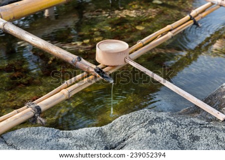 Traditional Japanese bamboo fountain dripping water with ripples in a basin