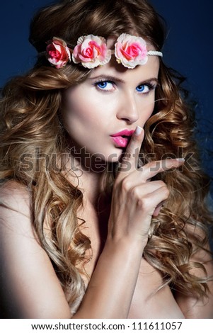 Portrait of young beautiful woman with long curly hair and flowers on her head .Hush babe with a White skin and red hair. Studio shoot, dark blue background.