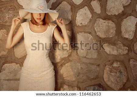 Fashion, Blonde  woman in lace dress  and hat posing against wall. Outdoor shot. Horizontal.