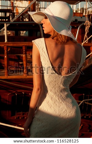 Back side view of lady with a hat and lace dress  near the wooden yachts . Vertical shot, outdoors.
