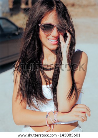 smiling young woman with long hair and sunglasses posing on a hot sunny day.